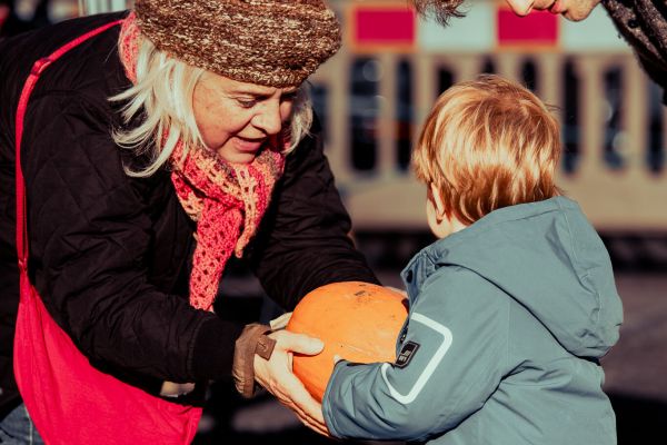 A woman hands a small child a pumpkin
