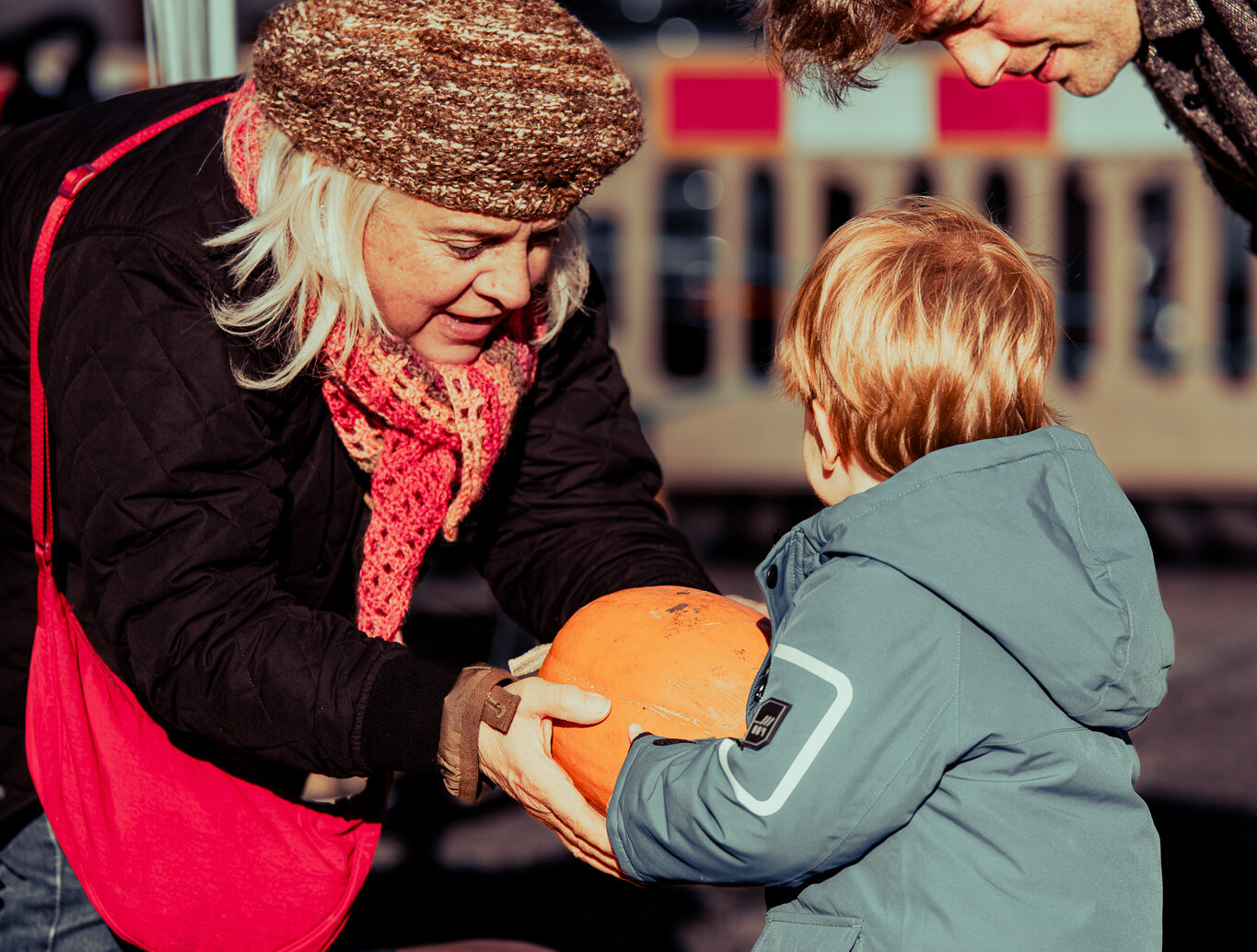 A woman hands a small child a pumpkin