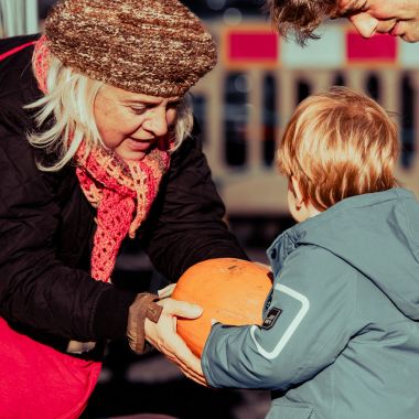 A woman hands a small child a pumpkin